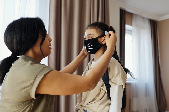 Mom helps his daughter wearing a mask