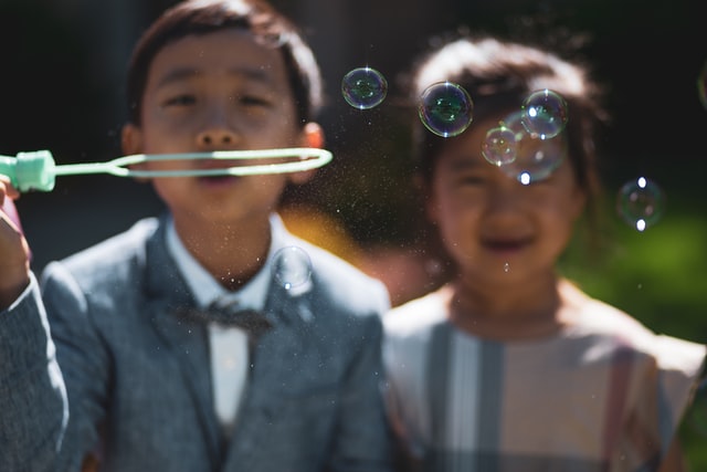 a little boy and girl wearing their formal suits and playing bubble